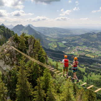 Deux adultes marchent sur la passerelle suspendue de la via ferrata de Charmey avec une vue sur la vallée