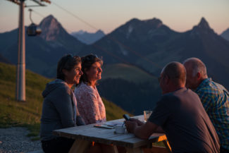Des amis boivent un verre sur une terrasse avec une vue sur un coucher de soleil depuis le sommet de Charmey