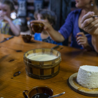 Des visiteurs sont assis à table avec un pot de crème double ainsi que du fromage é Charmey